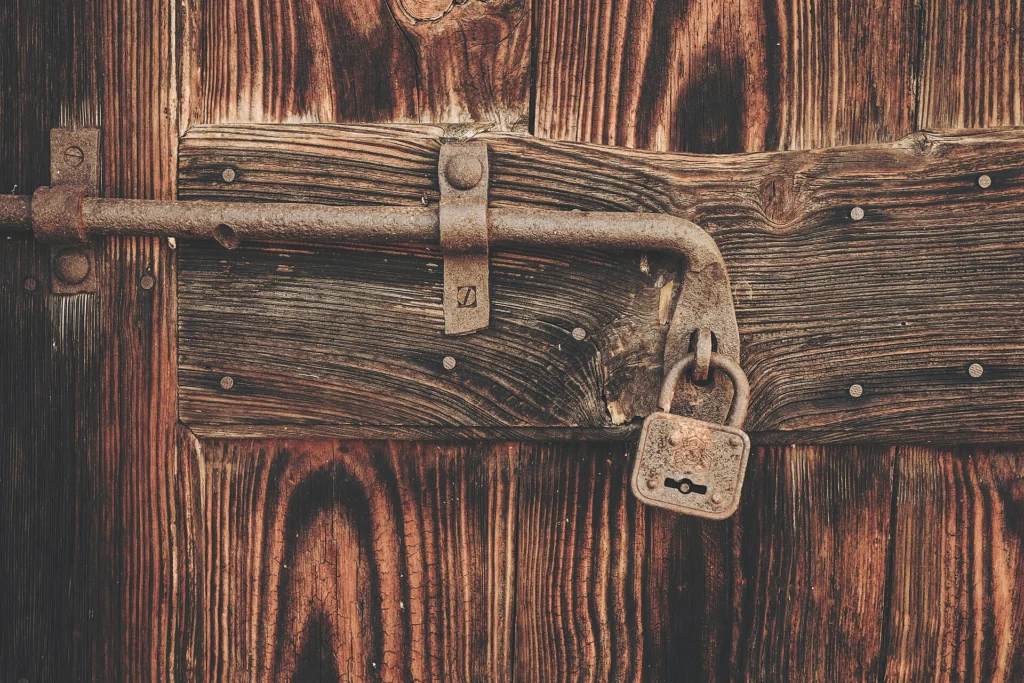 Old padlock securing a bolt on a rustic wooden door