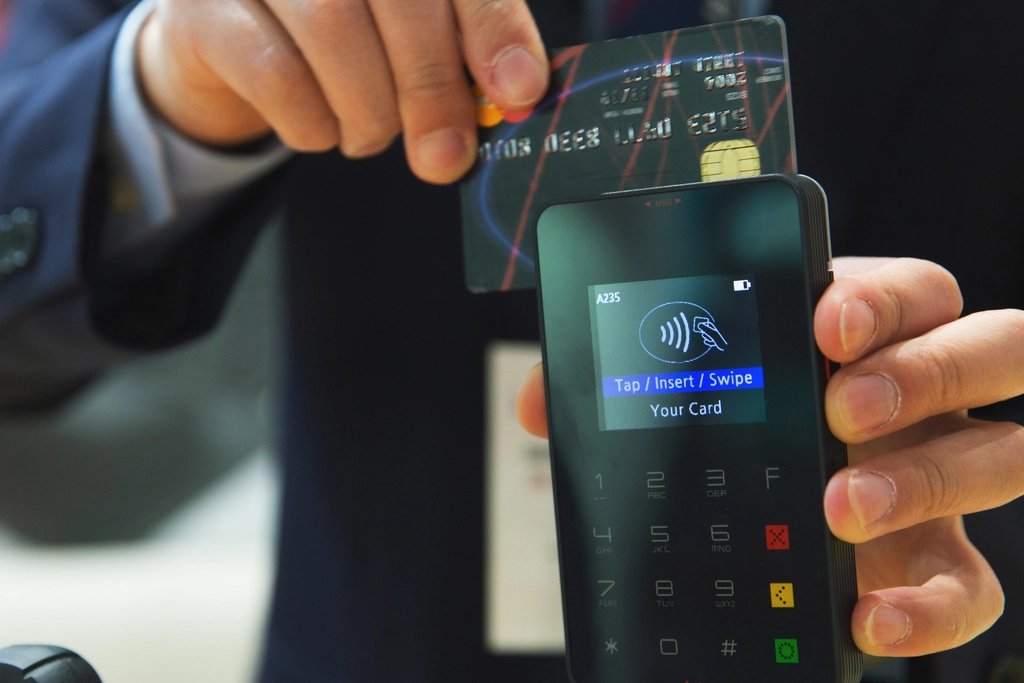 Card held next to a handheld payment terminal showing a tap or insert prompt