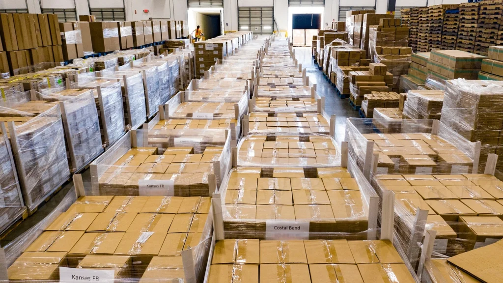 Rows of wrapped cardboard parcels on pallets down a warehouse aisle