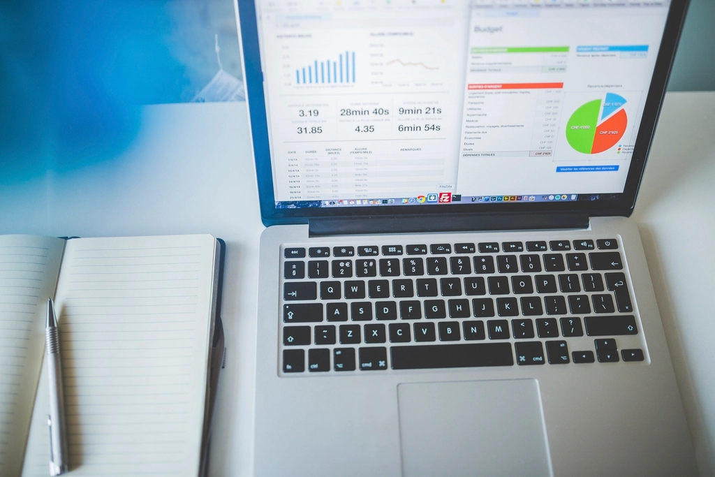 Laptop showing an analytics dashboard with charts next to a notebook
