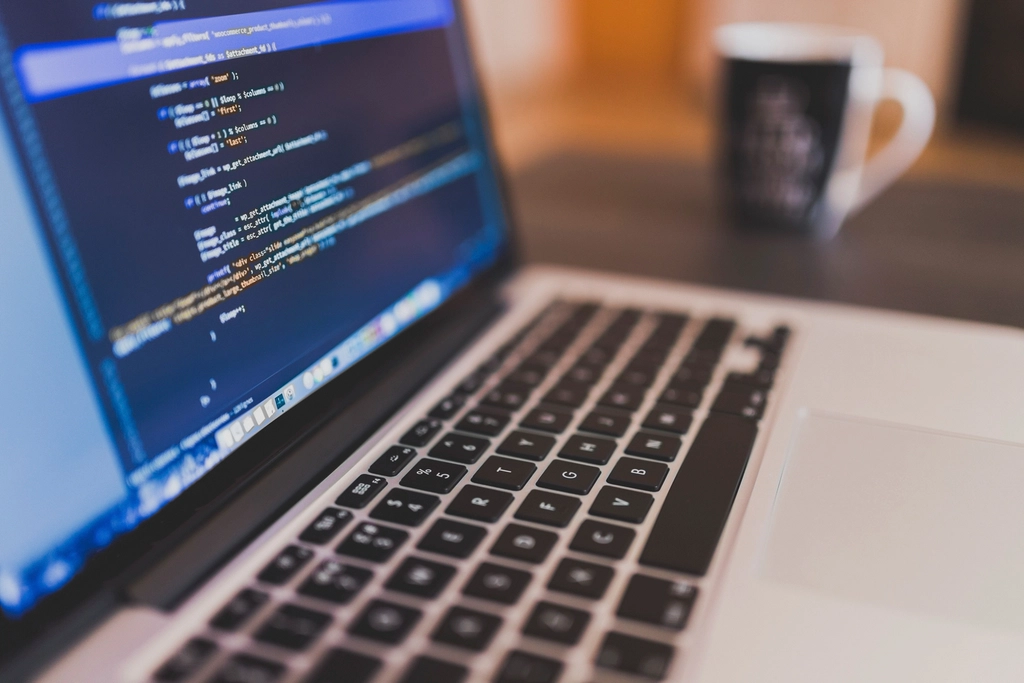 Laptop showing source code on a desk with a coffee mug in the background