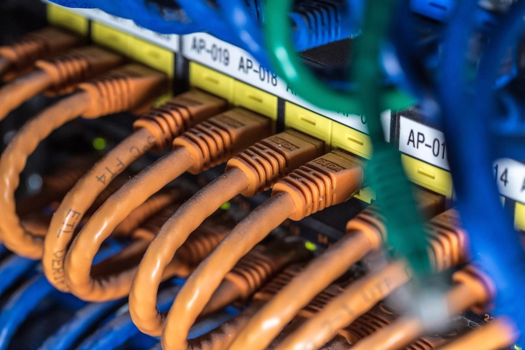 Orange network cables plugged into a labelled patch panel in a server rack