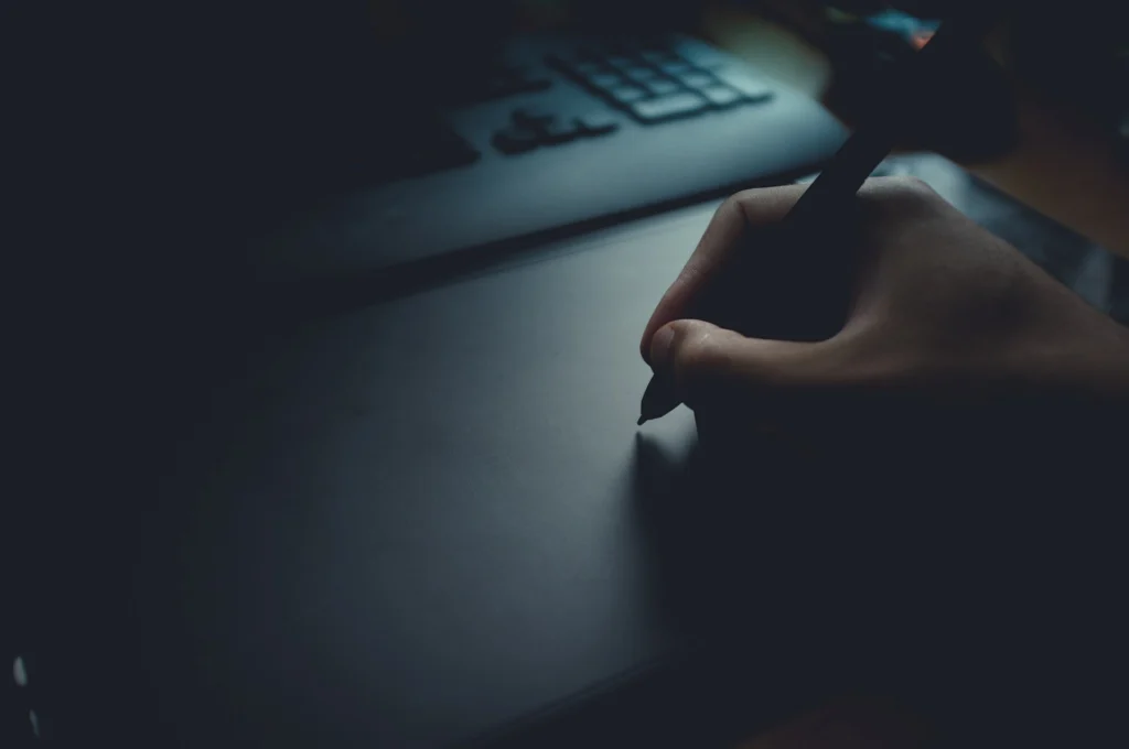 Designer's hand using a stylus on a graphics tablet in a dimly lit studio