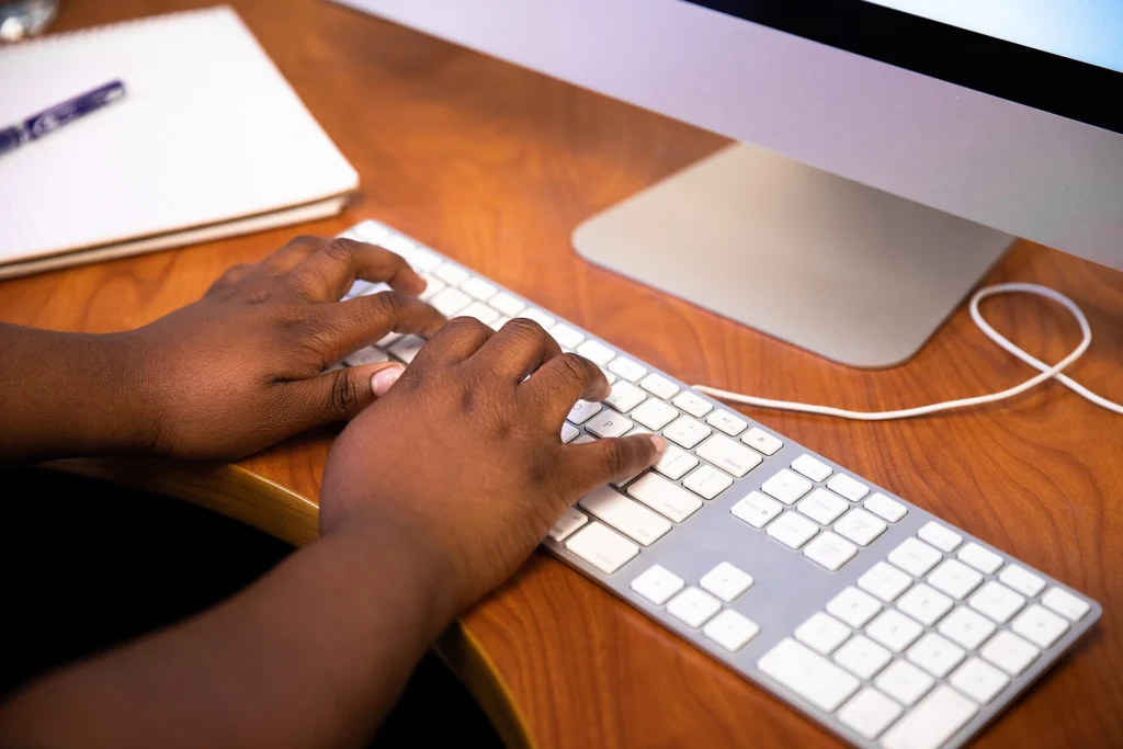 Hands typing on a white keyboard in front of a desktop monitor