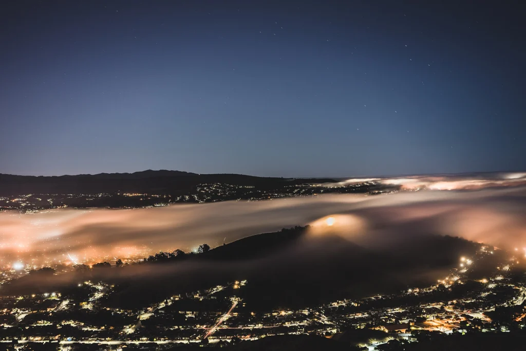 City lights glowing through fog below dark hills at night