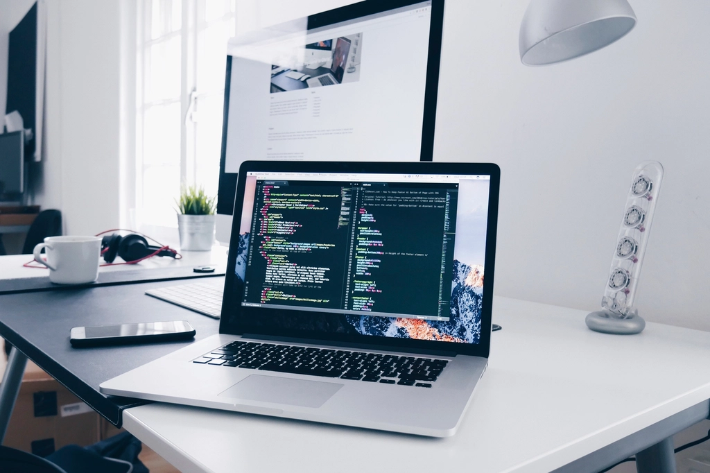 Flight: Laptop showing code on a minimal white desk next to a monitor
