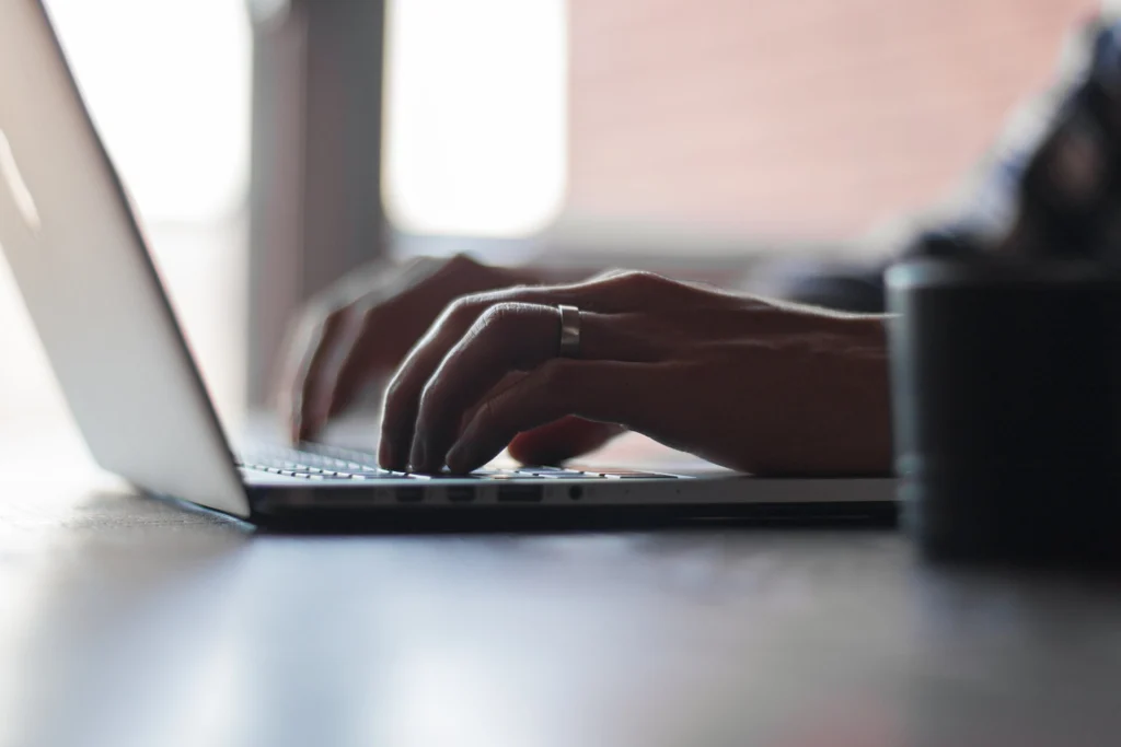 Close-up of hands typing on a laptop keyboard in soft daylight