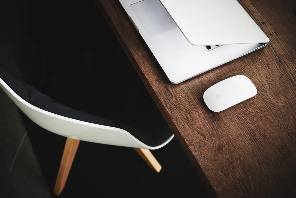 Half-closed laptop and a white mouse on a dark wooden desk