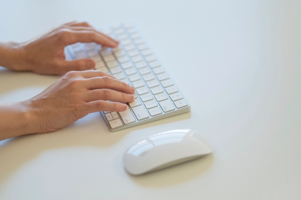 Hands typing on a white keyboard beside a computer mouse
