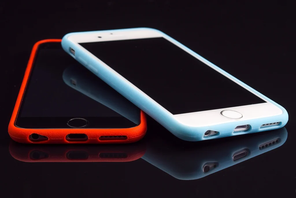 Two smartphones in red and light blue cases on a dark reflective surface