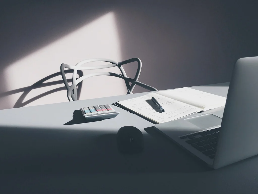 Minimal desk with a laptop, calculator and paper documents in soft light