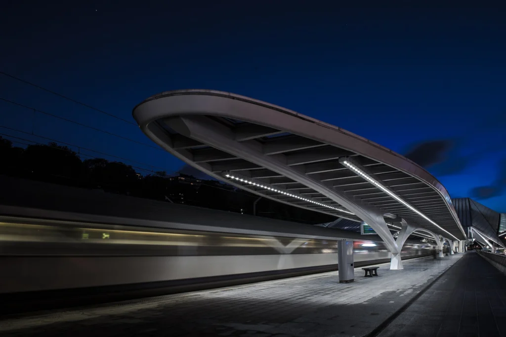 Motion-blurred train passing an illuminated modern station platform at night