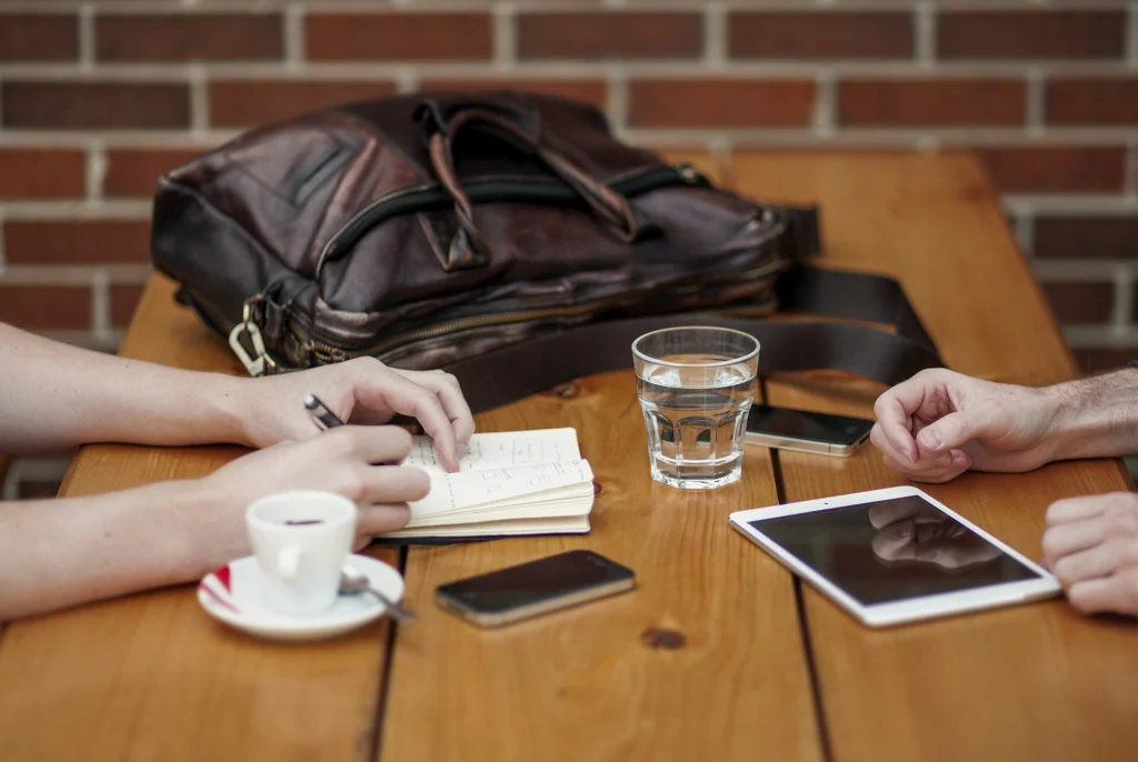 Two people planning at a cafe table with a notebook, smartphone and tablet