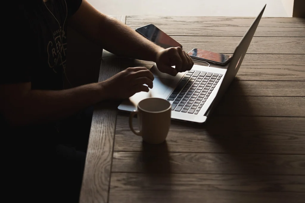 Mobile developer typing on a laptop with a smartphone and coffee on a wooden desk