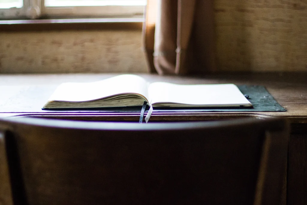 Open book lying on a wooden desk by an empty chair