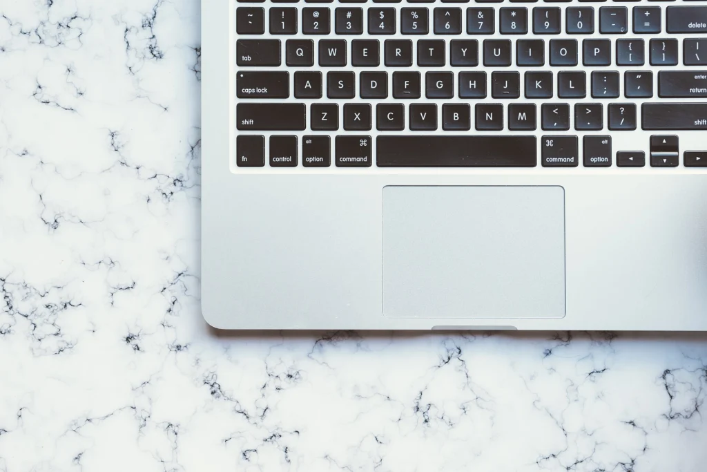 Silver laptop keyboard and trackpad on a white marble desk