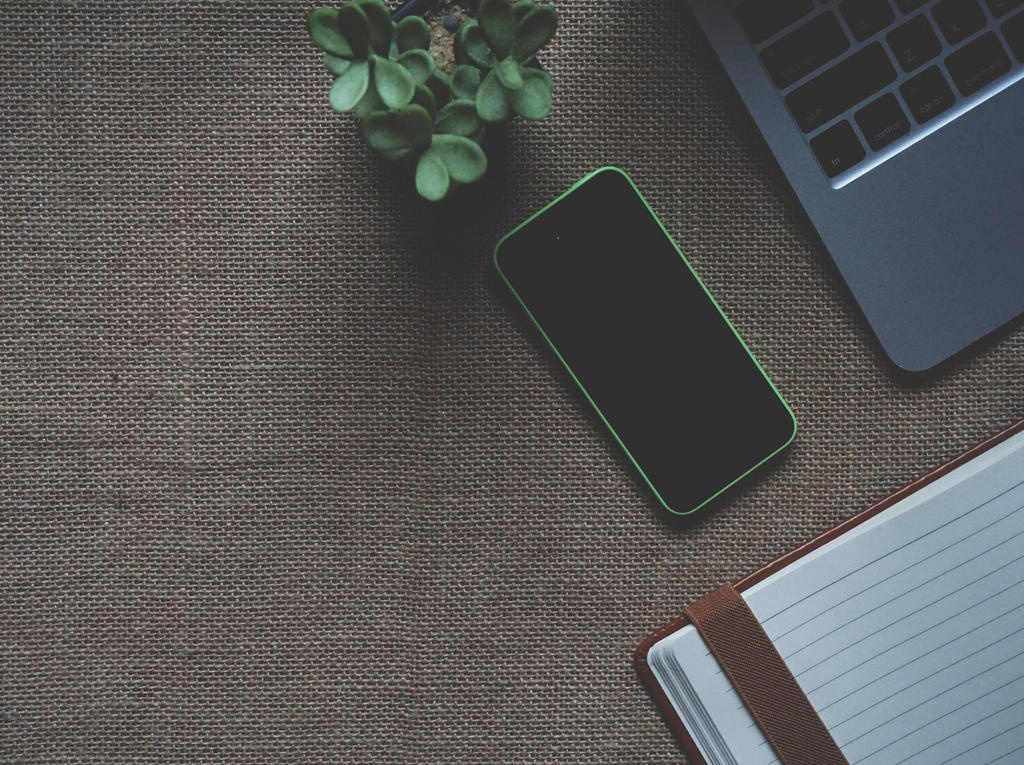 Smartphone and open notebook beside a laptop on a fabric desk