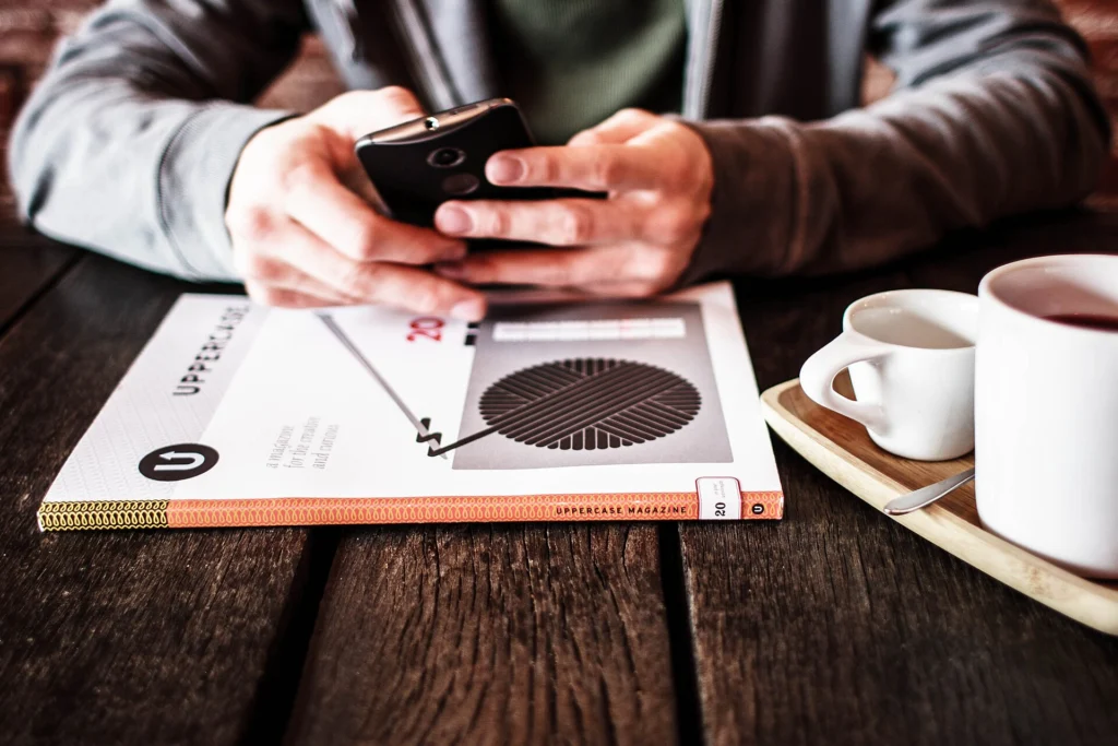 Person checking a smartphone at a cafe table next to cups of coffee
