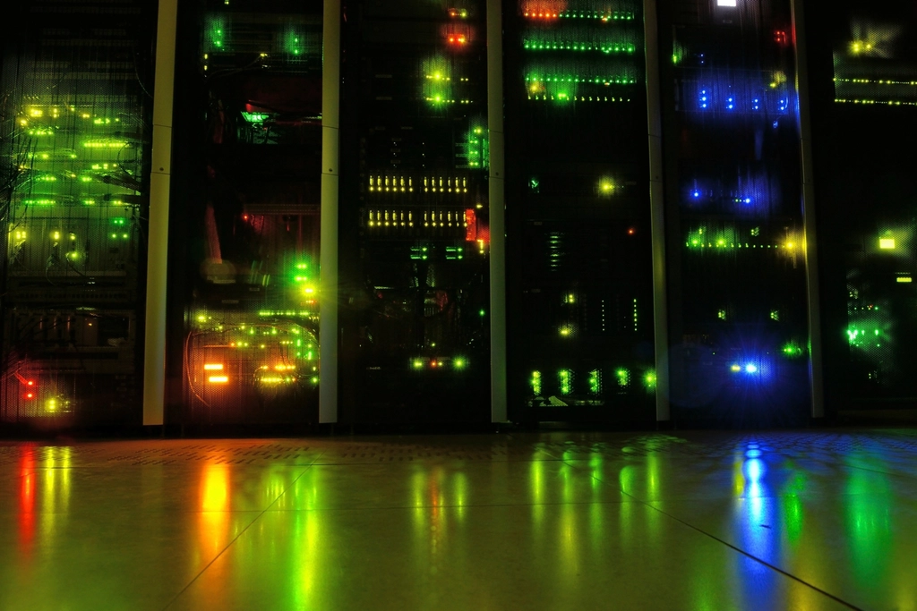 Server racks glowing with green, yellow and blue lights in a dark data center