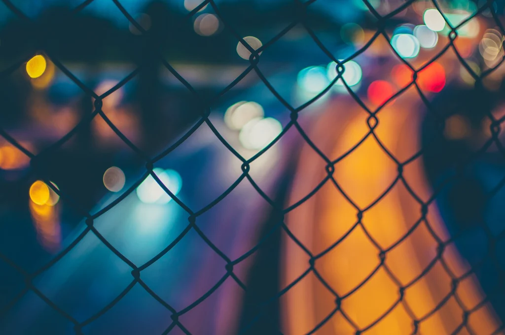 Rate: Chain-link fence in front of blurred red and blue city traffic lights at night