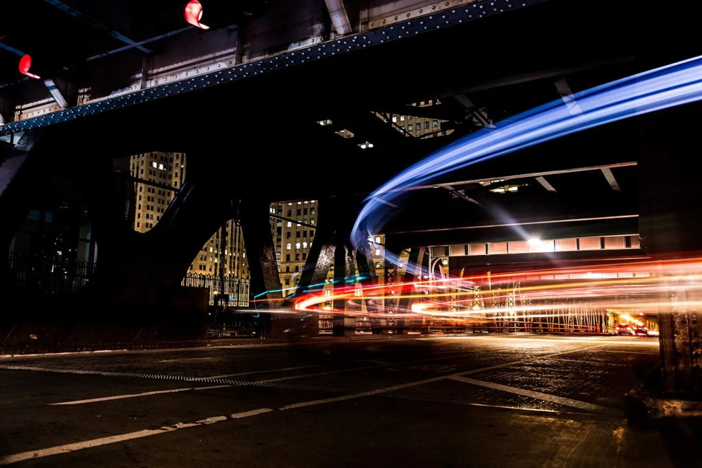 Long-exposure light trails of cars passing under a dark urban bridge