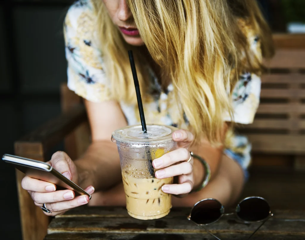 WebSocket: Person typing a chat message on a smartphone next to an iced coffee