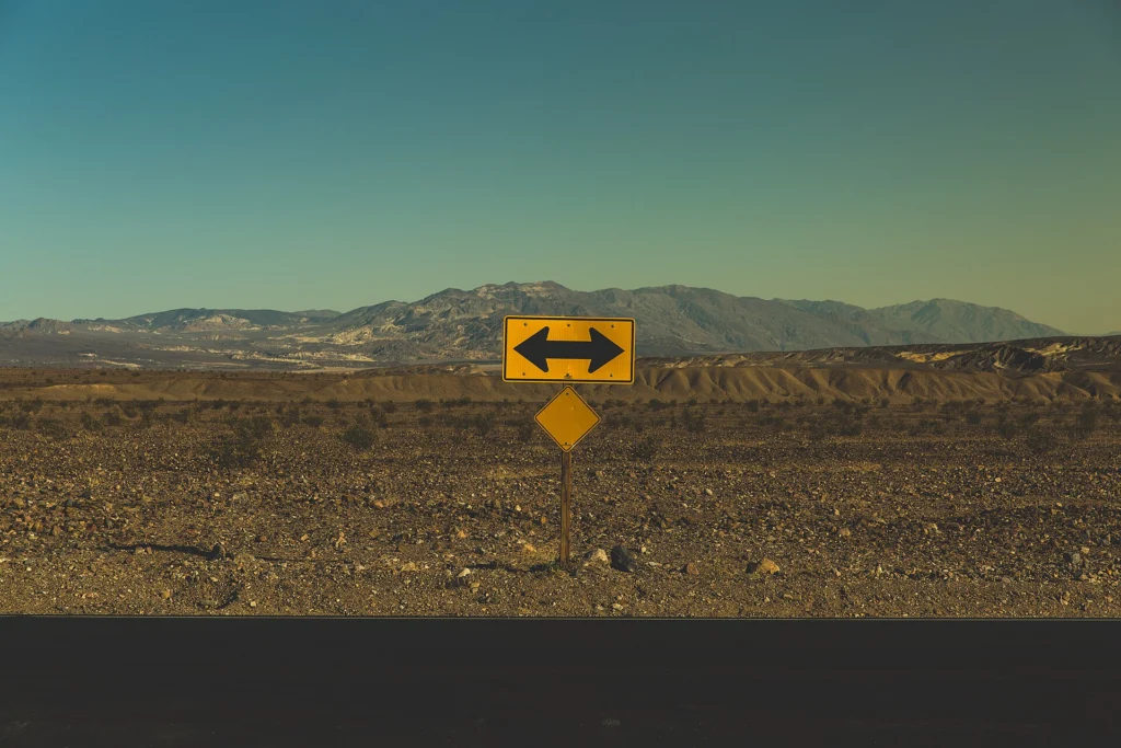 Database: Yellow road sign with arrows pointing in two directions in the desert