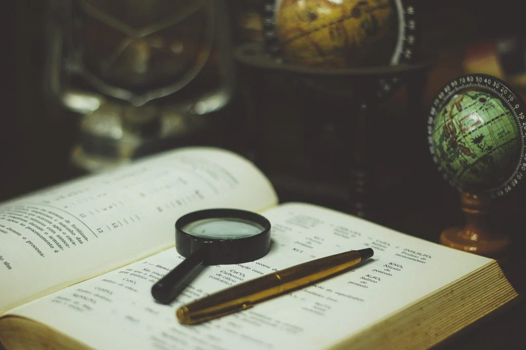 Site: Magnifying glass and pen resting on an open book next to a small globe