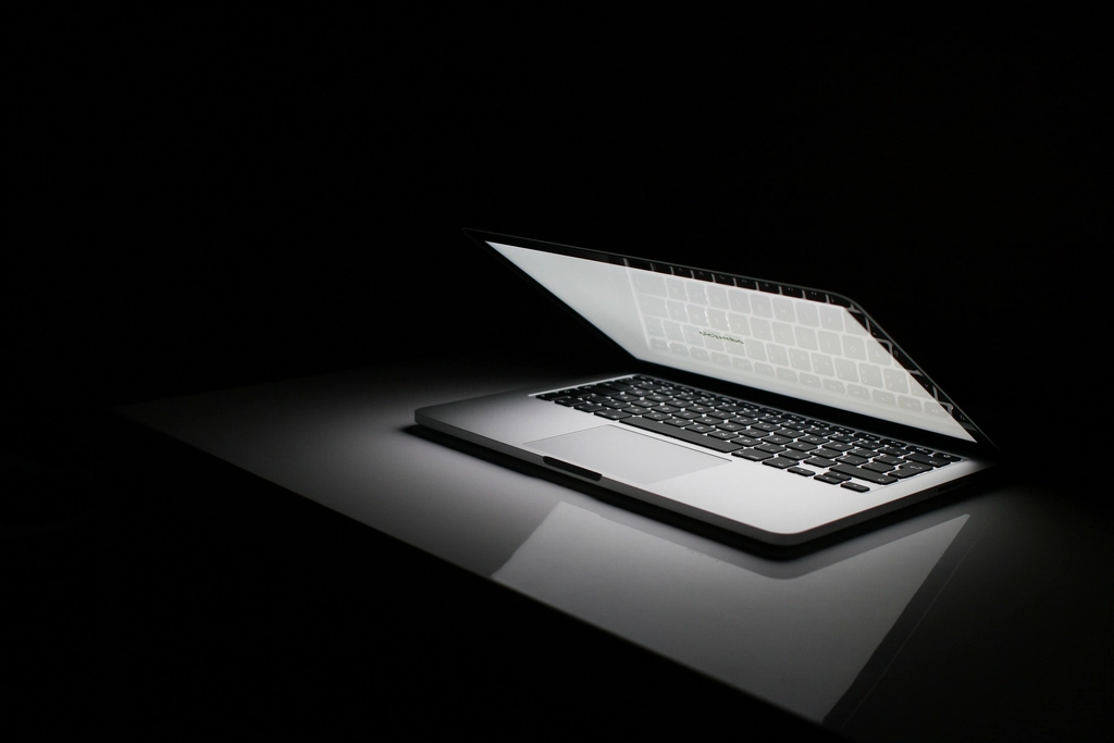 Half-open laptop with a glowing screen on a desk in a dark room