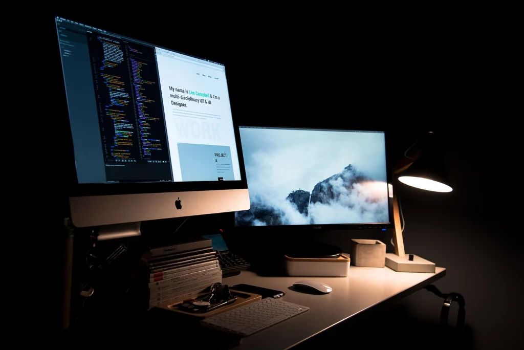 Static Site: Two monitors on a dark desk showing source code and a website preview