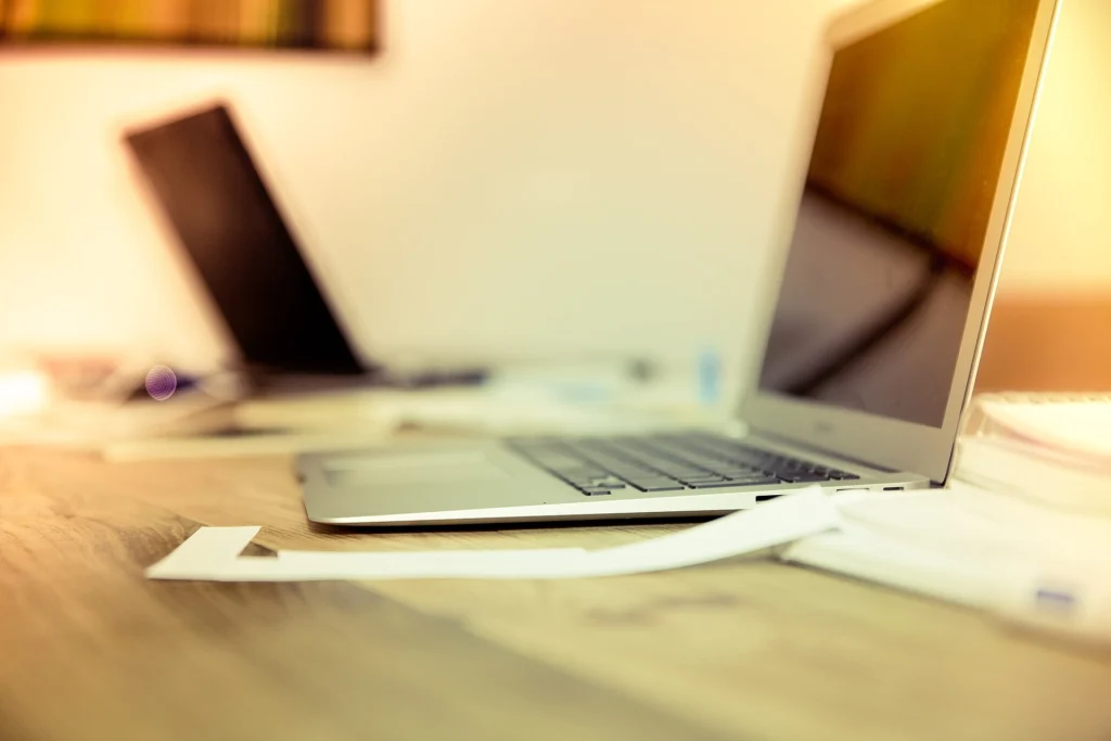 Open laptop on a bright wooden table with a second laptop in the background