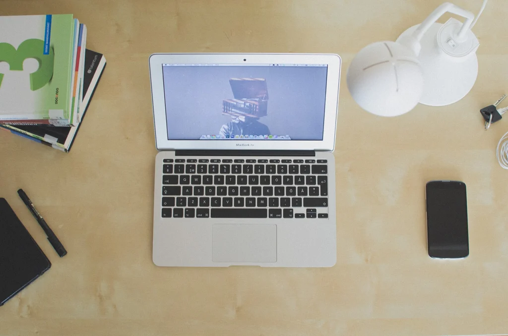 Maintenance: Top-down view of an open laptop on a wooden desk with a phone and books