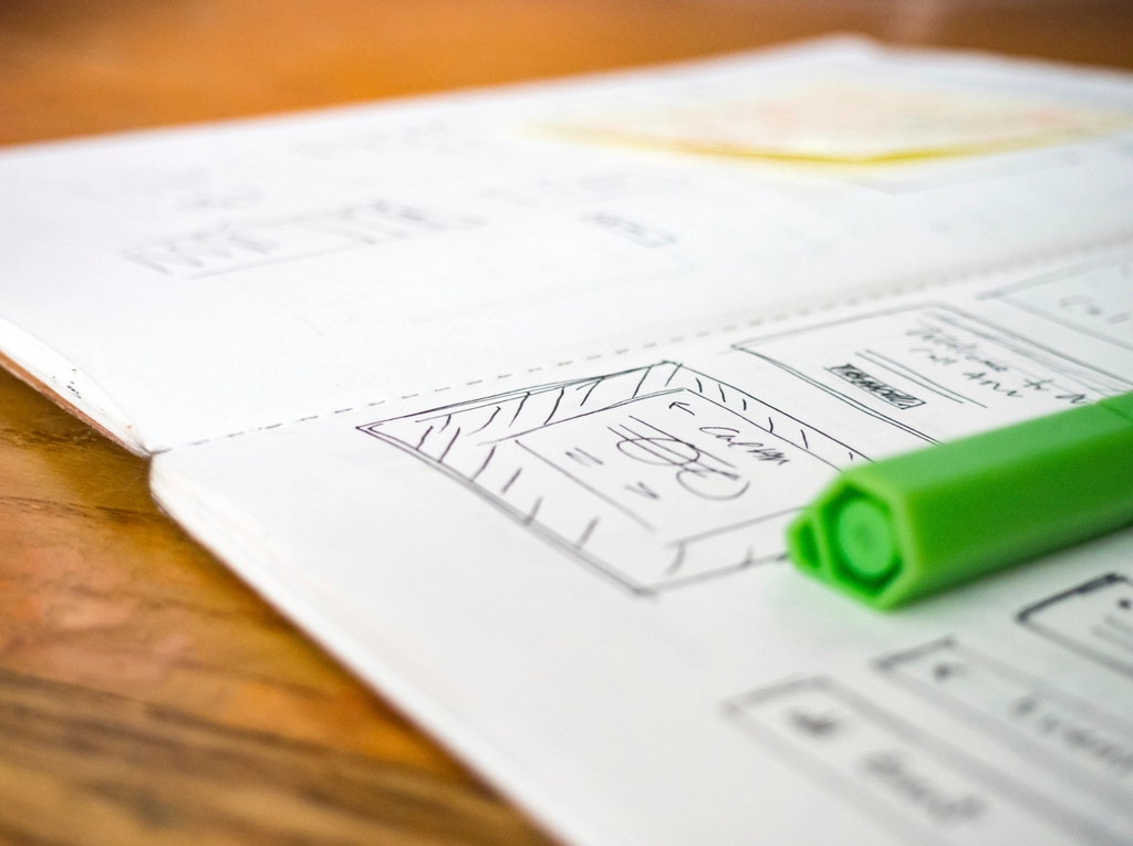 UX Design: Open notebook with hand-drawn interface wireframes and a green marker